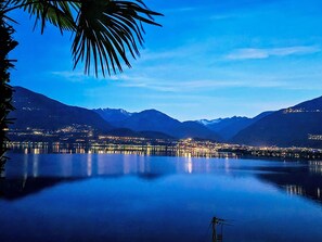 A calm lake with mountains in the background and a cityscape with lights reflecting on the water. - Vallegione Gerra by Interhome (Gerra)