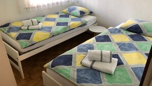 Due letti singoli con coperte colorate, un piccolo tavolo rotondo e una finestra con tende leggere.