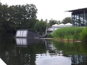 Ein Gebäude am Flussufer mit einem Anlegesteg, umgeben von Bäumen und Pflanzen.