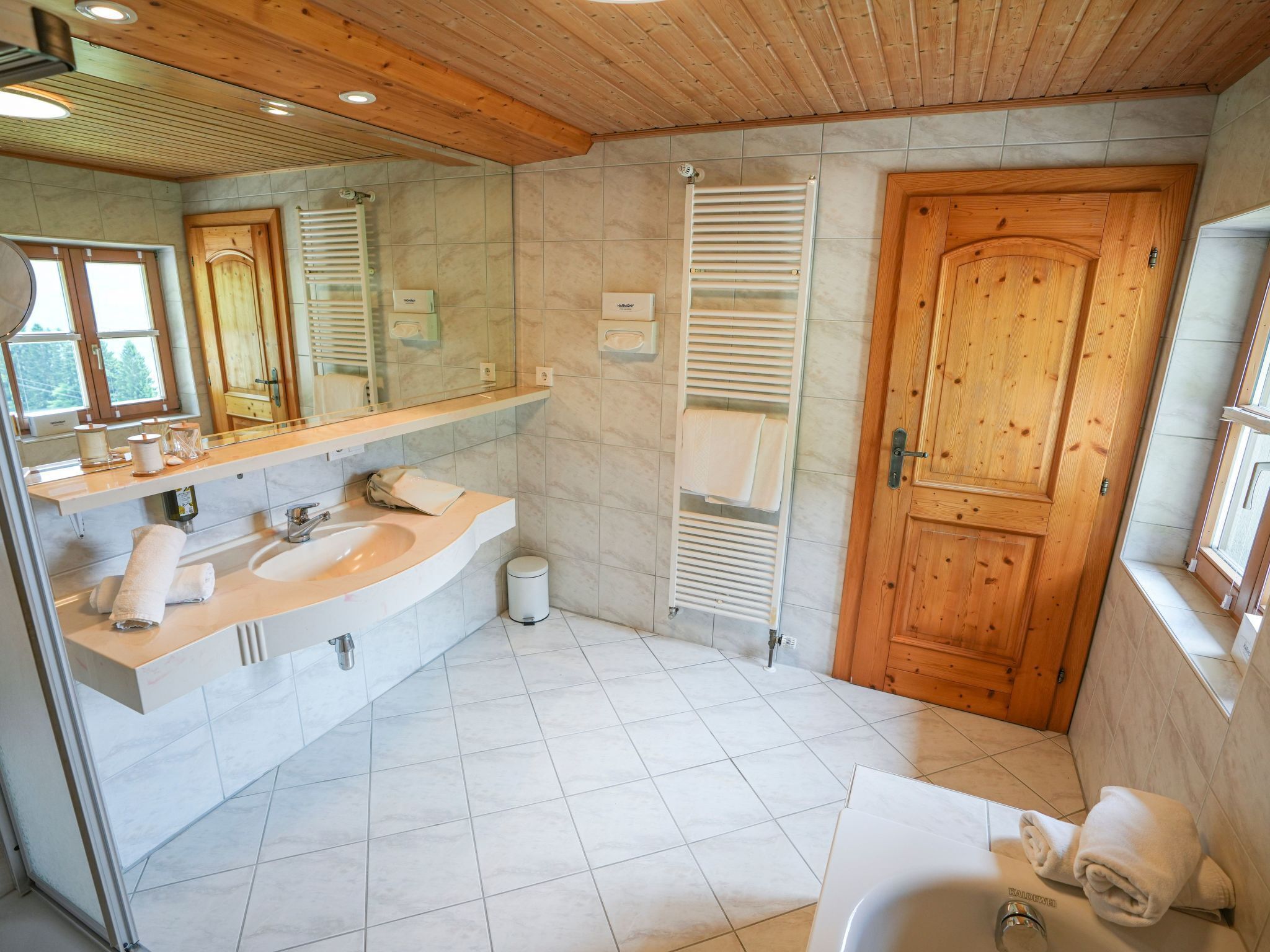 A modern bathroom with a wooden ceiling, a large mirror, a sink with a towel rack, a toilet, and a shower area.