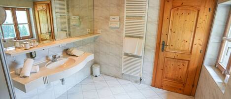A modern bathroom with a wooden ceiling, a large mirror, a sink with a towel rack, a toilet, and a shower area.