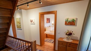 Eine Holztreppe führt zu einem Schlafzimmer mit einem Bett, einem Schminktisch und einem Bild an der Wand.