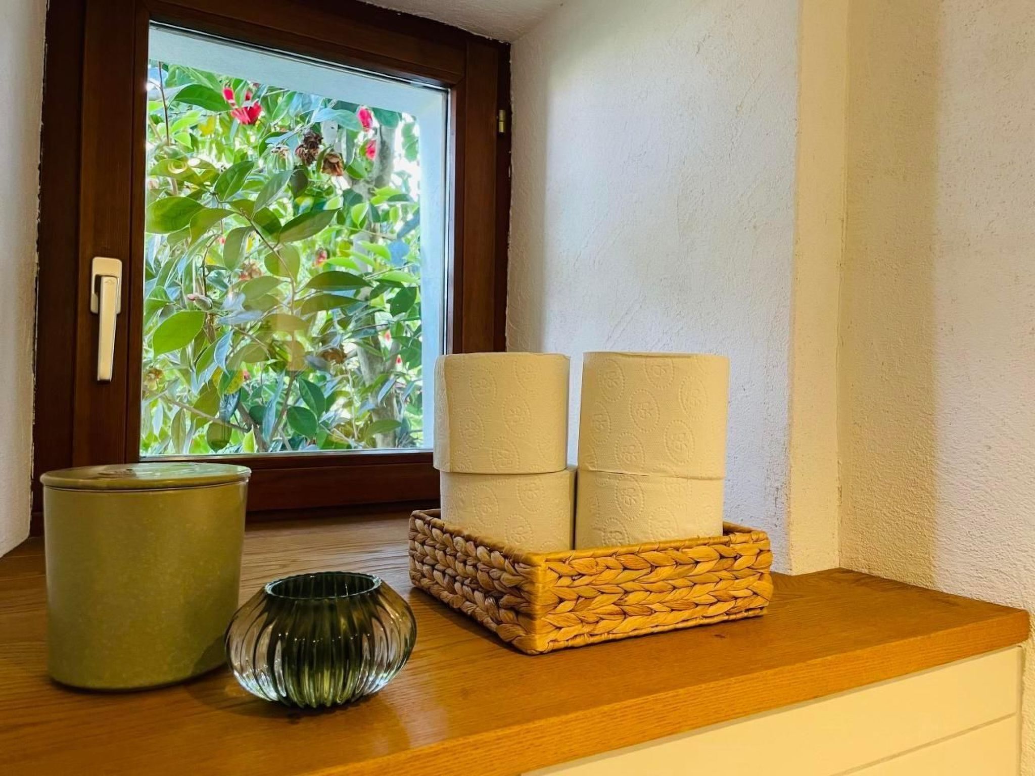 Une étagère en bois avec un récipient vert, un panier en osier contenant du papier toilette et un vase en verre.