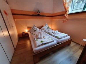 A bedroom with two beds, a nightstand, a small table, and a window with curtains. - Vacation home Sonja by Interhome (Frielendorf)