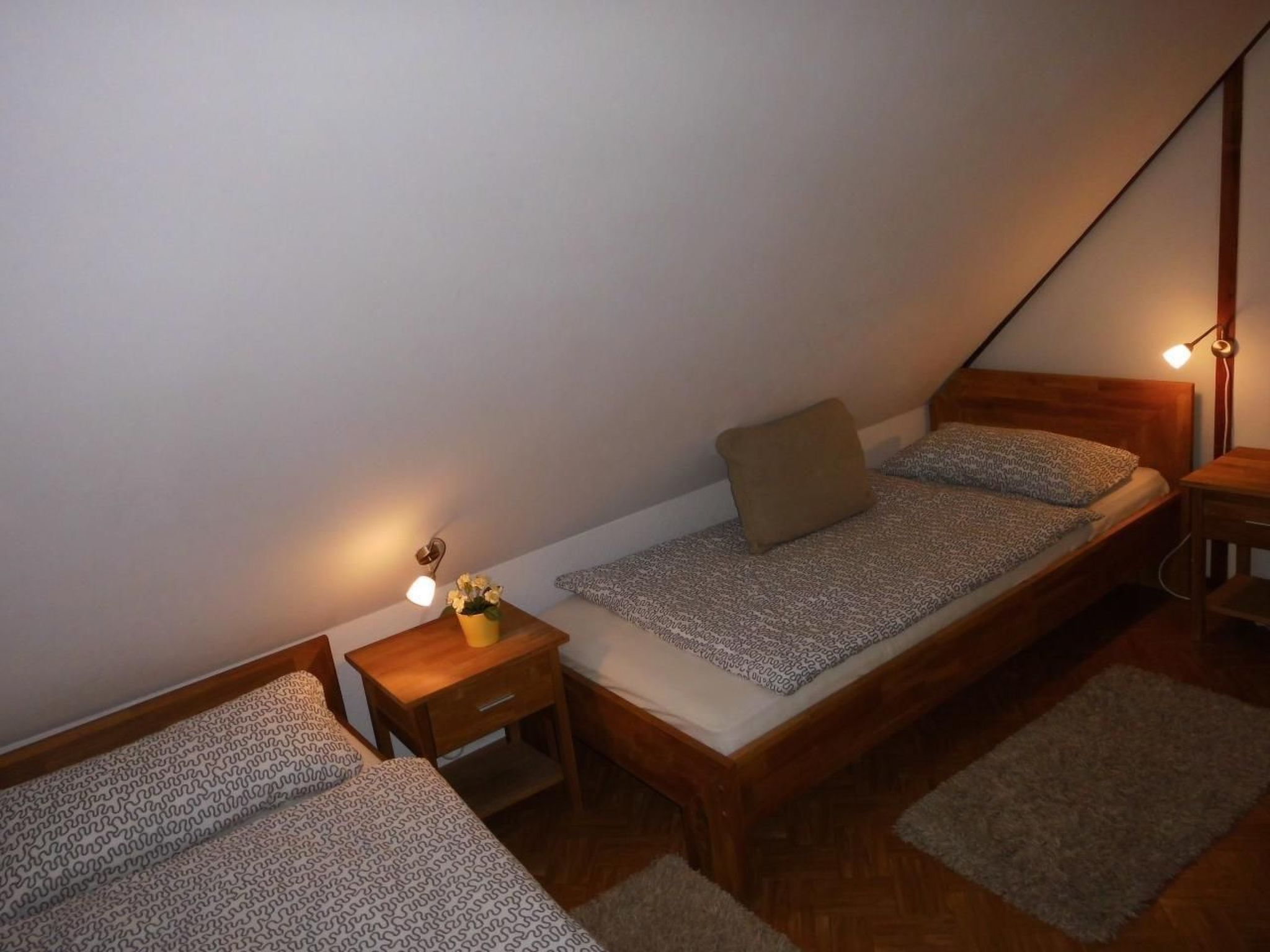 A small, triangular attic bedroom with a single bed, a nightstand, and a bedside table.