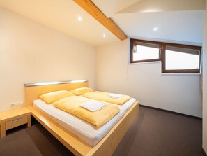 Ein Schlafzimmer mit einem Bett, einem Nachttisch, einem Fenster und einem Holzbalken an der Decke.