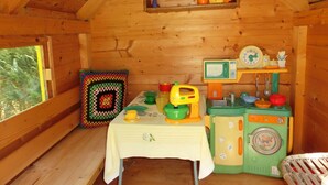 Interior de una cabaña de madera con una mesa dispuesta para una comida, una lavadora y un estante con utensilios de cocina.