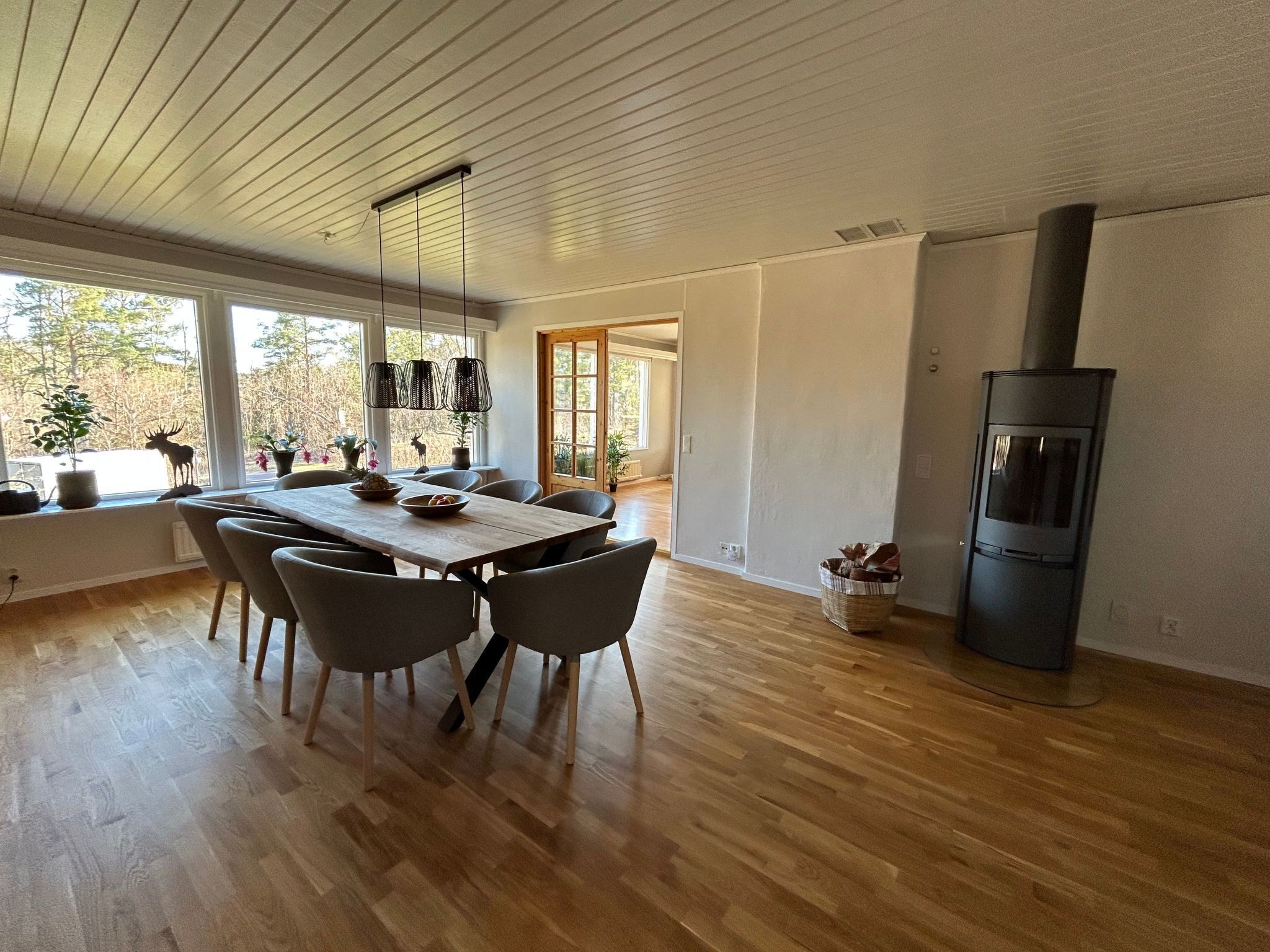 Un comedor moderno con una mesa y sillas de madera, ventanas amplias y un estufa de leña.