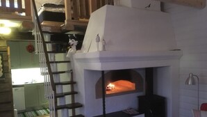 Een knus woongedeelte met een open haard, een trap en een keuken op de achtergrond.