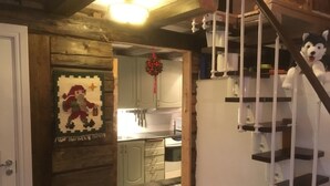 Een houten interieur met een trap, een keukenhoek en een wandplank met een knuffeldier.