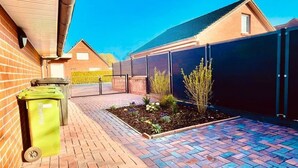 Un vialetto lastricato con un motivo a mattoni, un cestino verde e un'area giardino recintata.