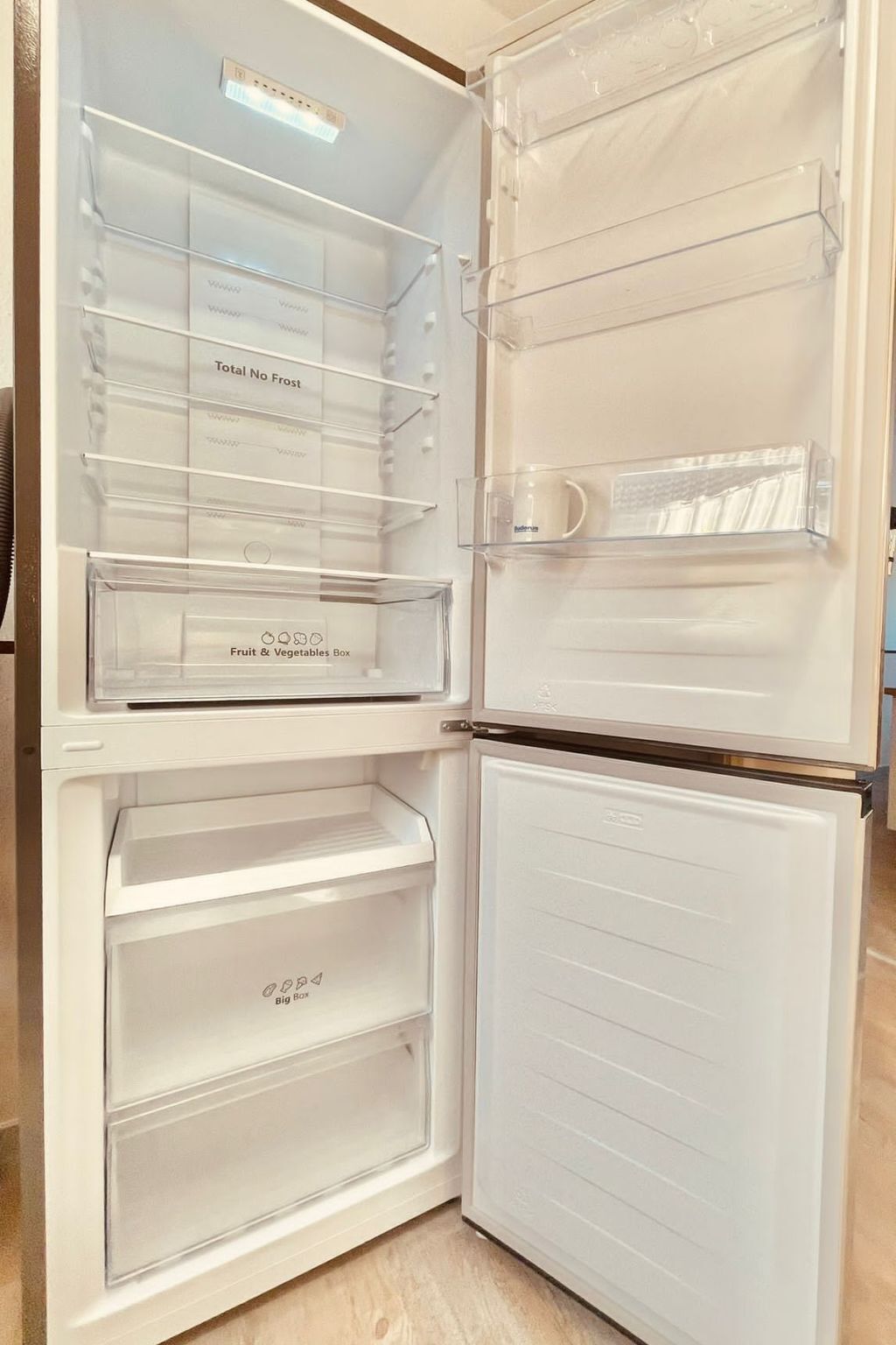 Un refrigerador abierto con compartimentos etiquetados, incluyendo una sección 'Total No Frost', una caja para 'Frutas y Verduras' y una sección 'Caja Grande'.