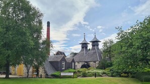 Een historisch gebouw met schoorsteen, een bord waarop "Strathhella Distillery" staat en een verzorgd gazon.
