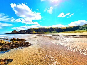 Ein Strand mit klarem Wasser, felsigem Ufer und Hügeln im Hintergrund.