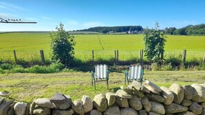 Twee gestreepte stoelen met uitzicht op een groen veld en bomen in de verte, tegen een stenen muur.