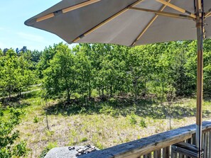 Eine Holzdielen-Terrasse mit einem großen Sonnenschirm, mit Blick auf eine bewaldete Gegend mit Bäumen und Sträuchern.