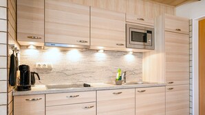 Una cocina moderna con armarios de madera clara, un microondas integrado y una cafetera de acero inoxidable.