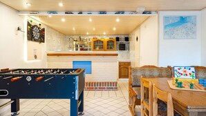 Un espace intérieur accueillant avec un baby-foot, un coin repas doté d’un échiquier et un espace cuisine équipé d’un jeu de fléchettes.