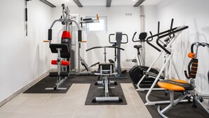 Une salle de sport équipée de divers appareils d’exercice, avec une fenêtre et un plafond aux poutres apparentes.