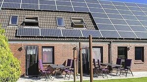 Un bâtiment doté d’un toit recouvert de panneaux solaires et d’un patio aménagé avec des sièges extérieurs.