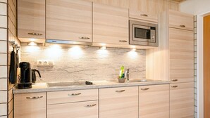 Une cuisine moderne avec des meubles en bois clair, un four à micro-ondes en acier inoxydable, une machine à café et un évier avec un robinet.
