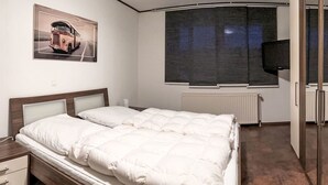 Et hotelværelse med en seng, et natbord, et fjernsyn, et stort vindue og et plakat på væggen.