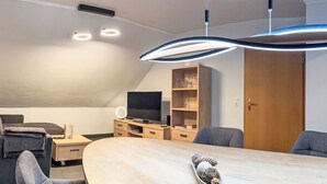 En moderne stue med et stort spisebord, et fladskærms-tv og en indbygget reol med glasvarer.
