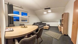 Et moderne loftsrum med spisebord, stole, sofa, fjernsyn og bogreol.