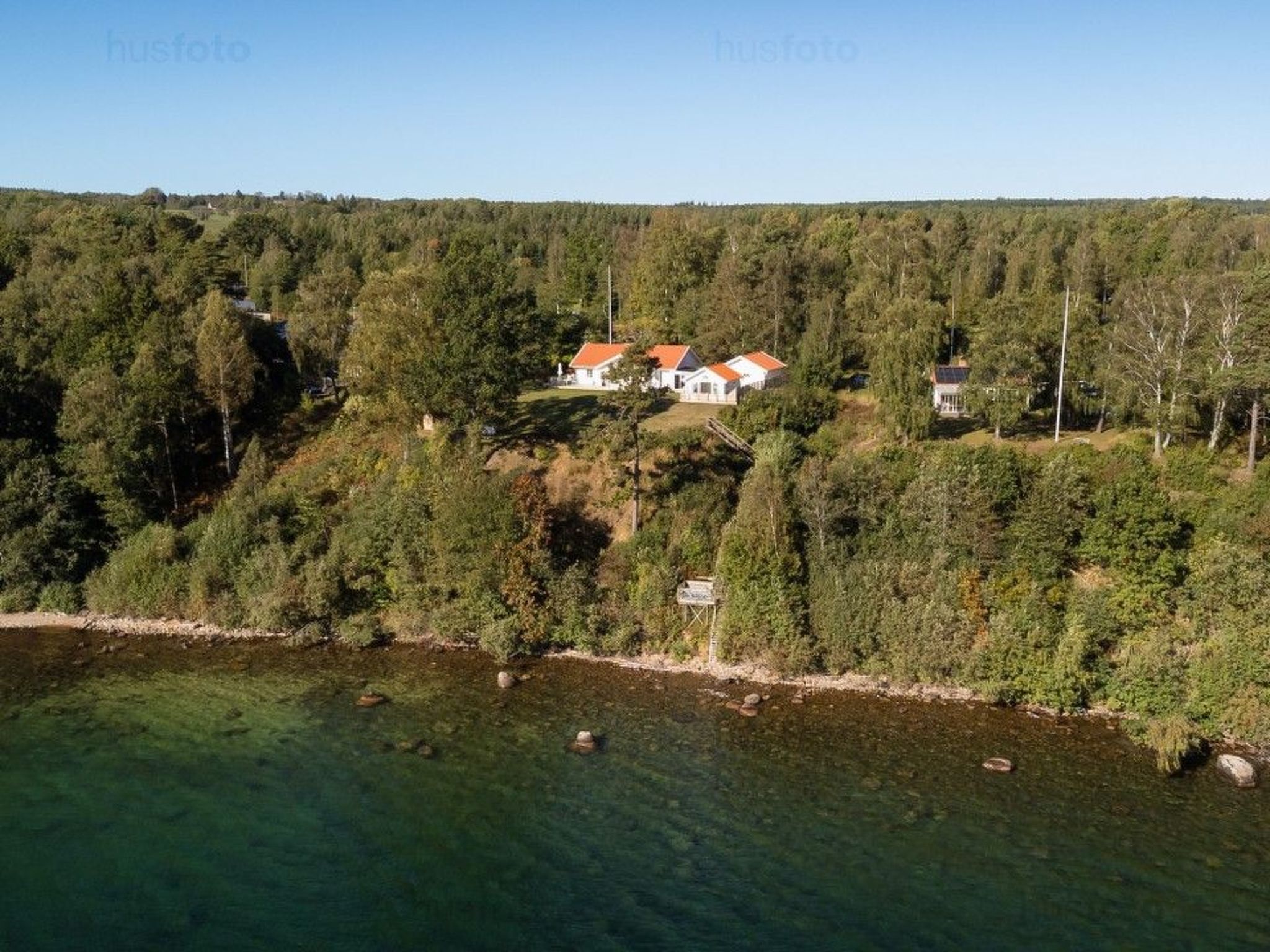 A cluster of houses with red roofs nestled among dense trees, overlooking a clear body of water.