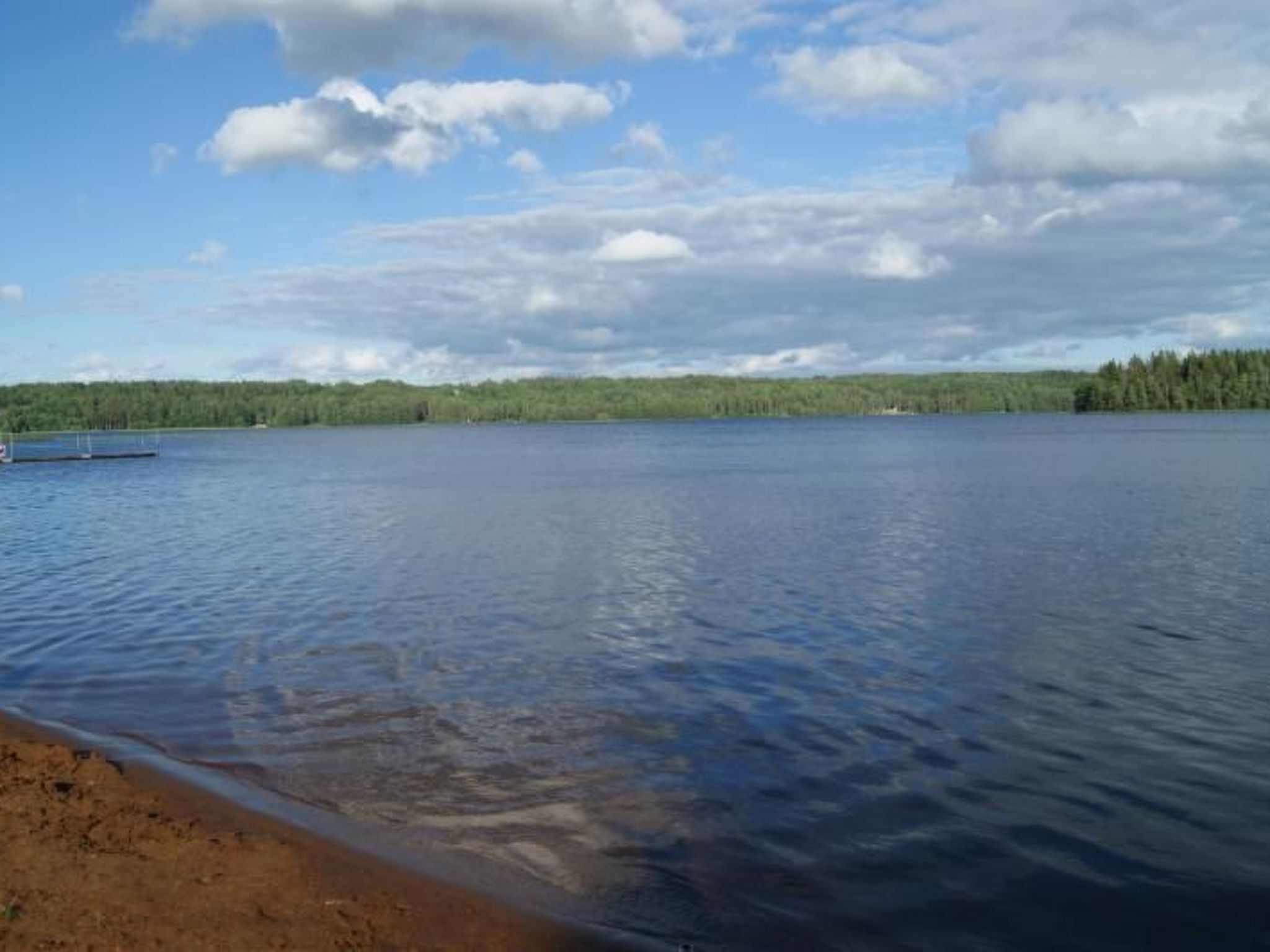 Un lago tranquilo con un muelle y una orilla cubierta de bosque.