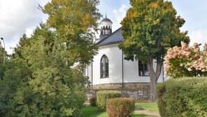 A white church with a steeple, surrounded by lush greenery and trees. - Typisch schwedisches Ferienhaus mit Garten by Interhome (Vena)
