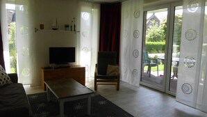 A living room with a TV, a sofa, a coffee table, and a chair. There is a sliding glass door leading to an outdoor area with a table and chairs. - Barrierefreie FeHausHälfte mit Terrasse. by Interhome (Hasselberg)