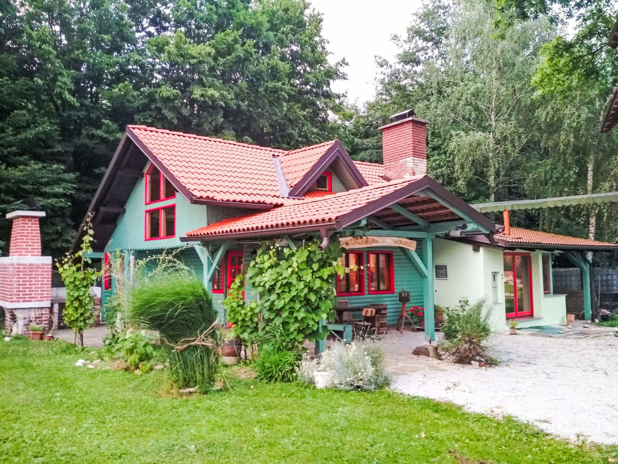 Una casa de dos pisos con techo de tejas rojas, una chimenea de ladrillo y un jardín con diversas plantas.