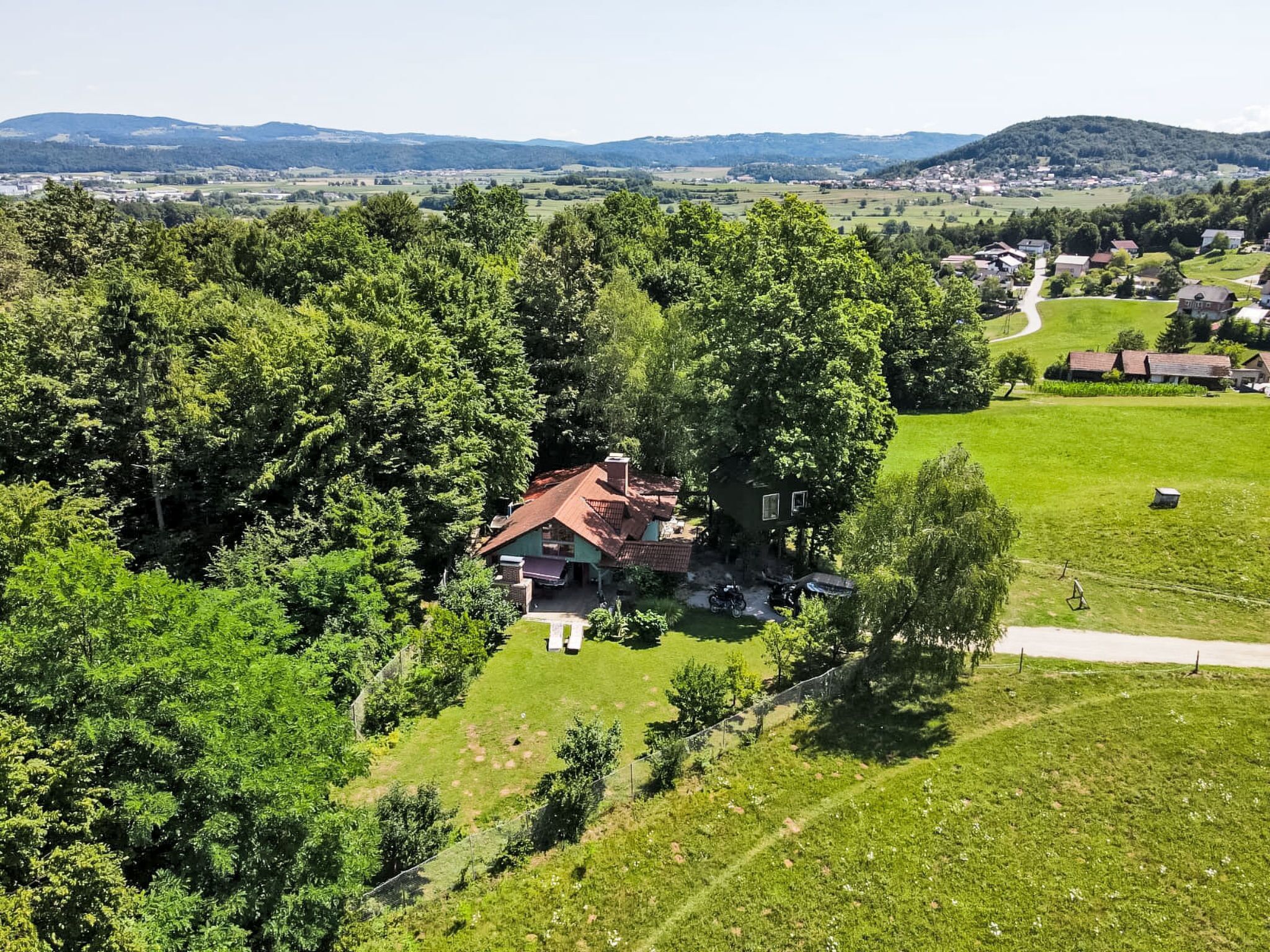 A house surrounded by dense trees, with a clear view of the surrounding landscape and distant hills.