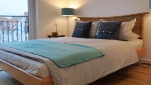 A hotel room with a large bed, a bedside table with a lamp, and a view of buildings outside the window. - Sonnendeck in Eckernförde by Interhome (Eckernförde)
