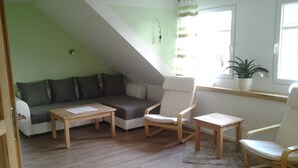 Una sala de estar acogedora con un sofá, dos sillones, una mesita y una ventana con una planta en el alféizar.