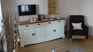 A living room with a white cabinet, a black chair, a TV, and a wooden shelf with books and decorative items. - Festung zu Ketghe by Interhome (Kettig)