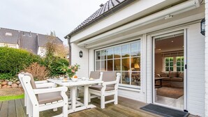 A patio with a white table and chairs, a glass door leading inside, and a view of the garden. - Horstweg in Westerland by Interhome (Archsum)