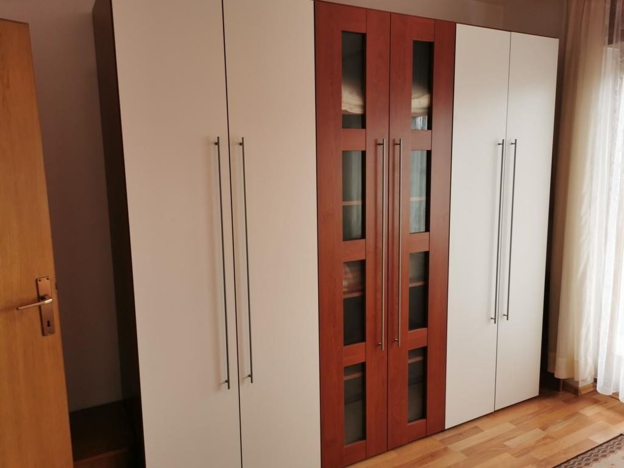 Habitación con armario que combina puertas blancas y de madera, con paneles de vidrio y tiradores metálicos.