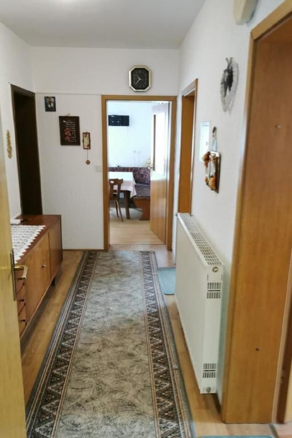 En hall med en mönstrad matta, ett element och en klocka på väggen.