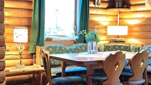 A cozy cabin interior with a wooden dining table, four chairs, a bench, and a window with curtains.