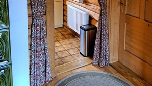 A wooden cabin interior with a kitchen area, including a stove, hanging pots, and a radiator.