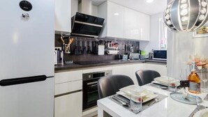 Une cuisine moderne avec des meubles blancs, un four encastré et un coin repas avec une table blanche mise pour deux personnes.