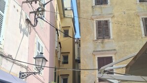 Une rue étroite, bordée de bâtiments des deux côtés, avec un lampadaire et un étal de fruits et légumes proposant une variété de produits.