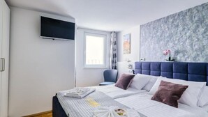 Une chambre d’hôtel avec un grand lit, un téléviseur fixé au mur, une fenêtre avec des rideaux et un papier peint à motifs floraux sur le mur.