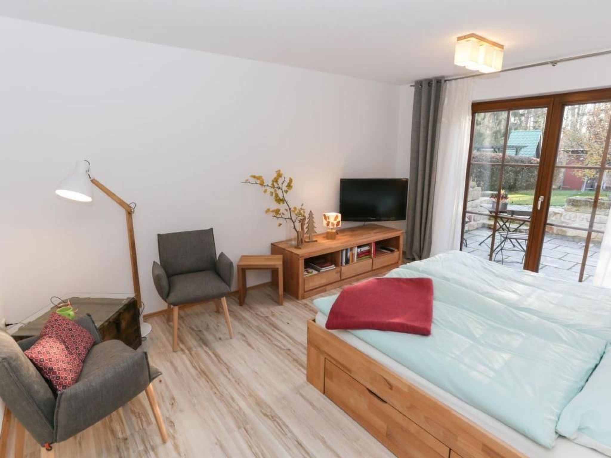 Ein Schlafzimmer mit Bett, Stuhl, Schreibtisch, Fernseher und Fenster.