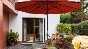A patio with a red umbrella, a wooden table, and chairs, surrounded by potted plants and a stone wall. - Apartment Grete by Interhome (Erfurt)