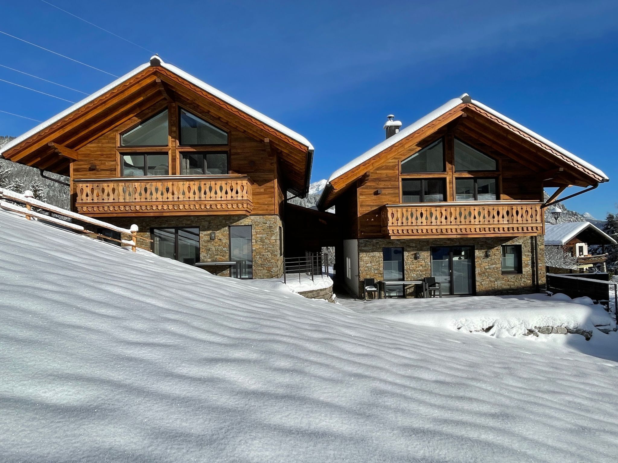 Eine moderne Holzchalet mit großen Fenstern und Balkonen, gelegen an einem verschneiten Hang.