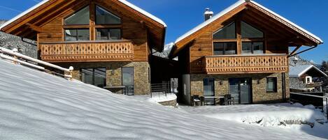 Eine moderne Holzchalet mit großen Fenstern und Balkonen, gelegen an einem verschneiten Hang.