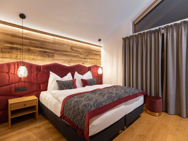A modern bedroom with a wooden headboard, a bed with patterned bedding, bedside lamps, and a window with curtains. - Edelstein by Interhome (Forstau)